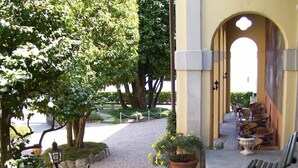A courtyard with a gravel path, potted plants, a bench, and outdoor seating. - Villa La Mirabella (Griante)