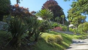 A garden with a variety of plants, a stone wall, and a staircase leading up. - Villa La Mirabella (Griante)