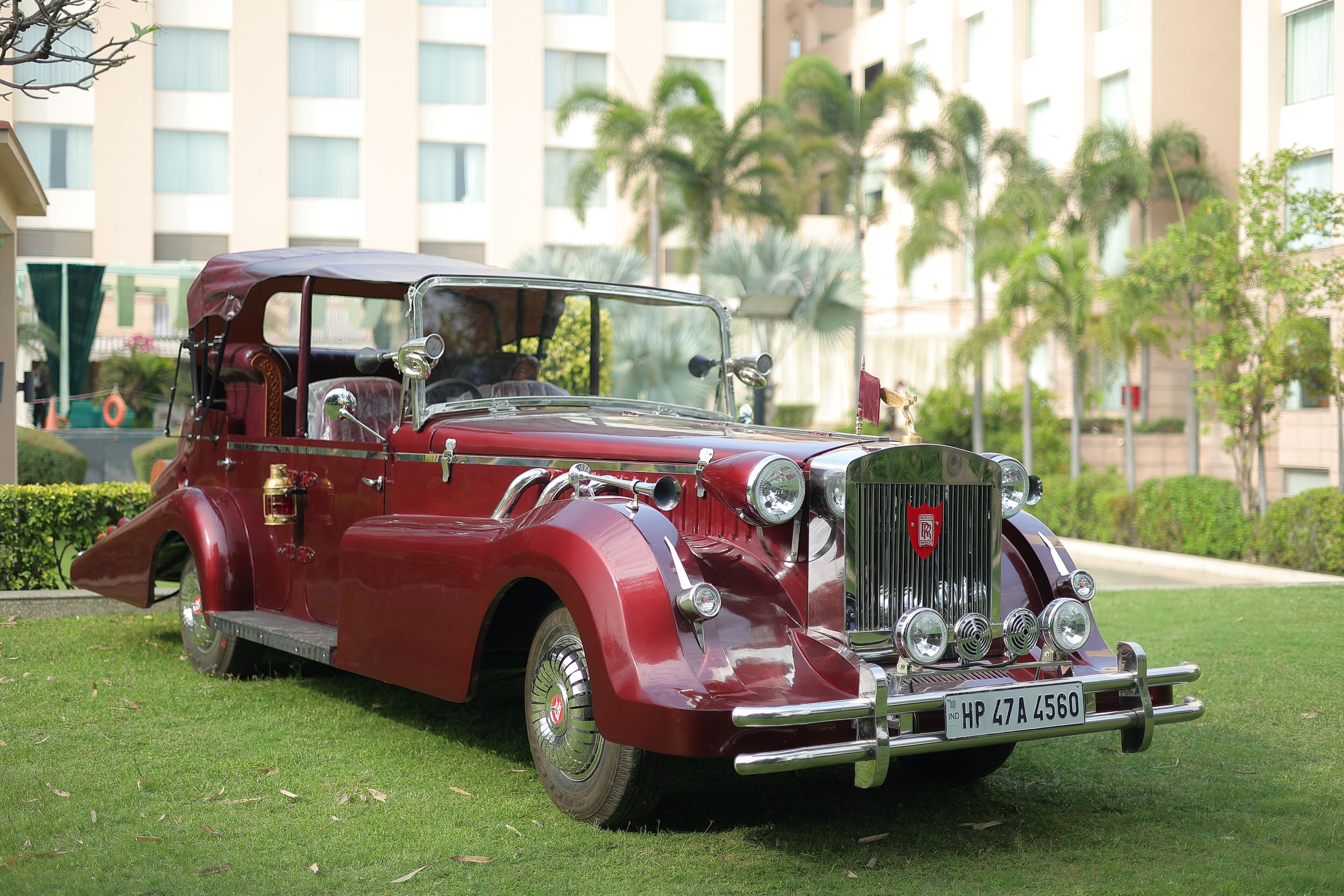 A vintage red car parked on a grassy area with a building in the background.