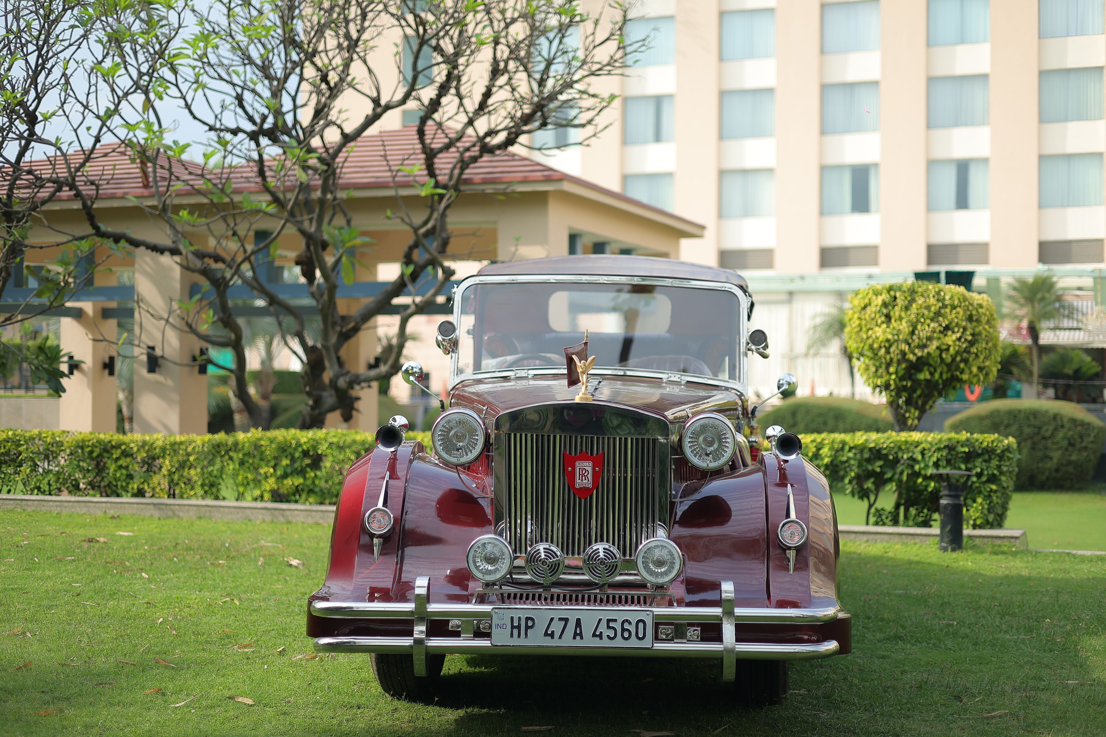 A vintage car parked on a grassy area with a building in the background.