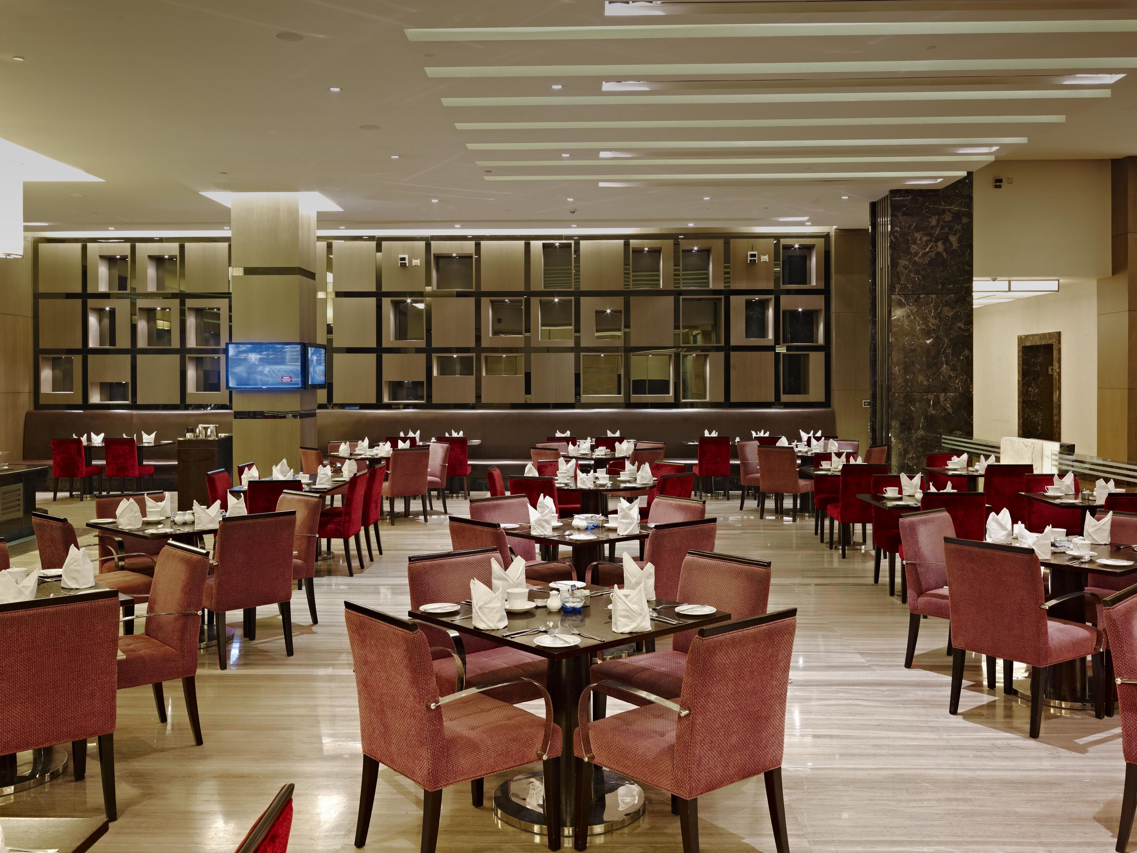 A spacious dining area with multiple tables and chairs, a television mounted on the wall, and a modern ceiling design.