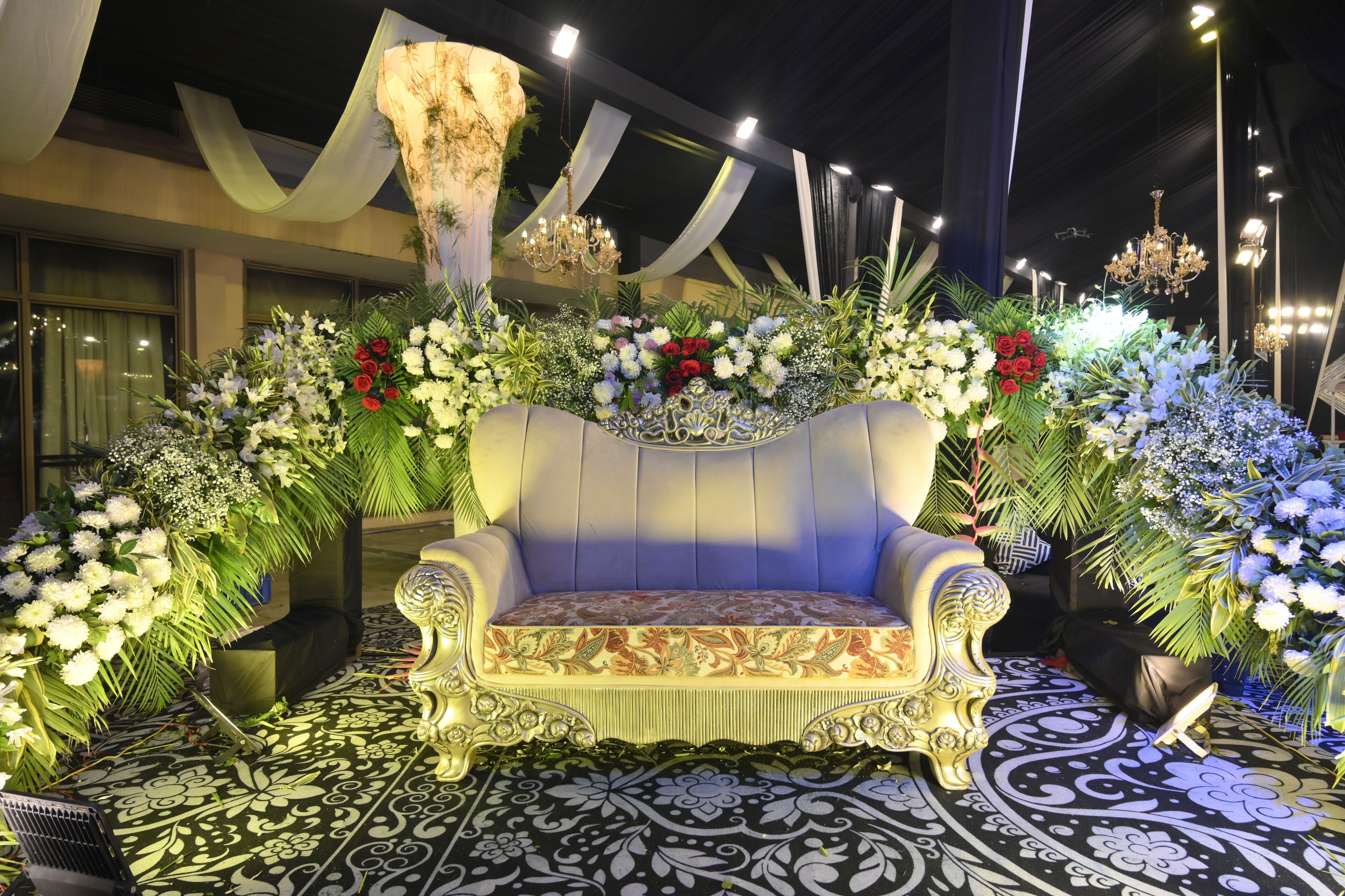A luxurious sofa set surrounded by elaborate floral arrangements and a patterned floor.