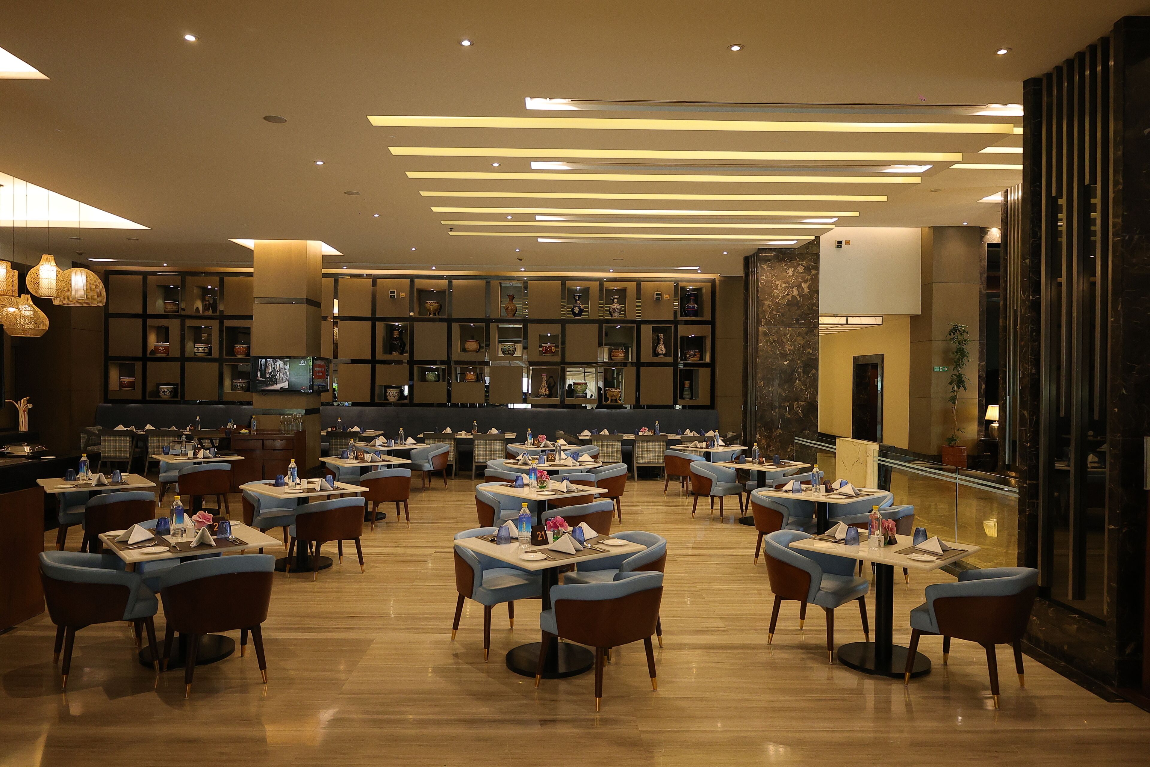 A spacious restaurant with multiple tables and chairs, a bar area, and a view of the city through large windows.