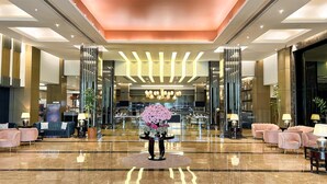 A spacious lobby with a central floral arrangement, high ceilings with recessed lighting, and a polished marble floor.