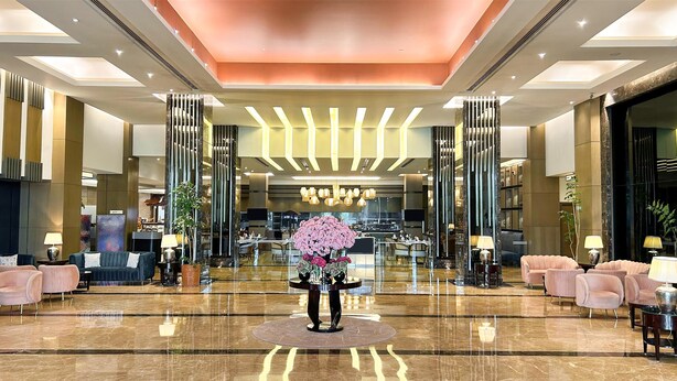 A spacious lobby with a central floral arrangement, high ceilings with recessed lighting, and a polished marble floor. - Radisson Blu Hotel Rudrapur (Kichha)