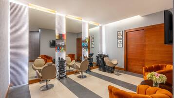 A salon with multiple hairdressing stations, a reception area with a wooden door, and a mirror reflecting the interior.