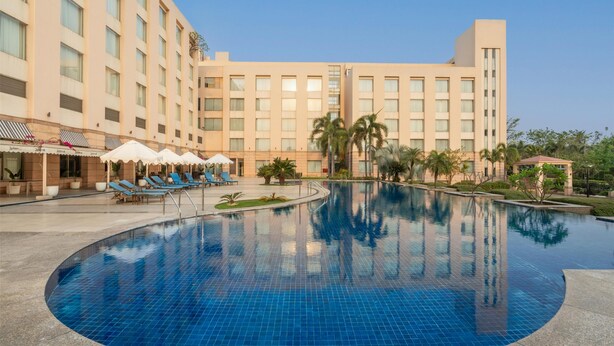 A hotel with a large swimming pool, sun loungers, and palm trees.