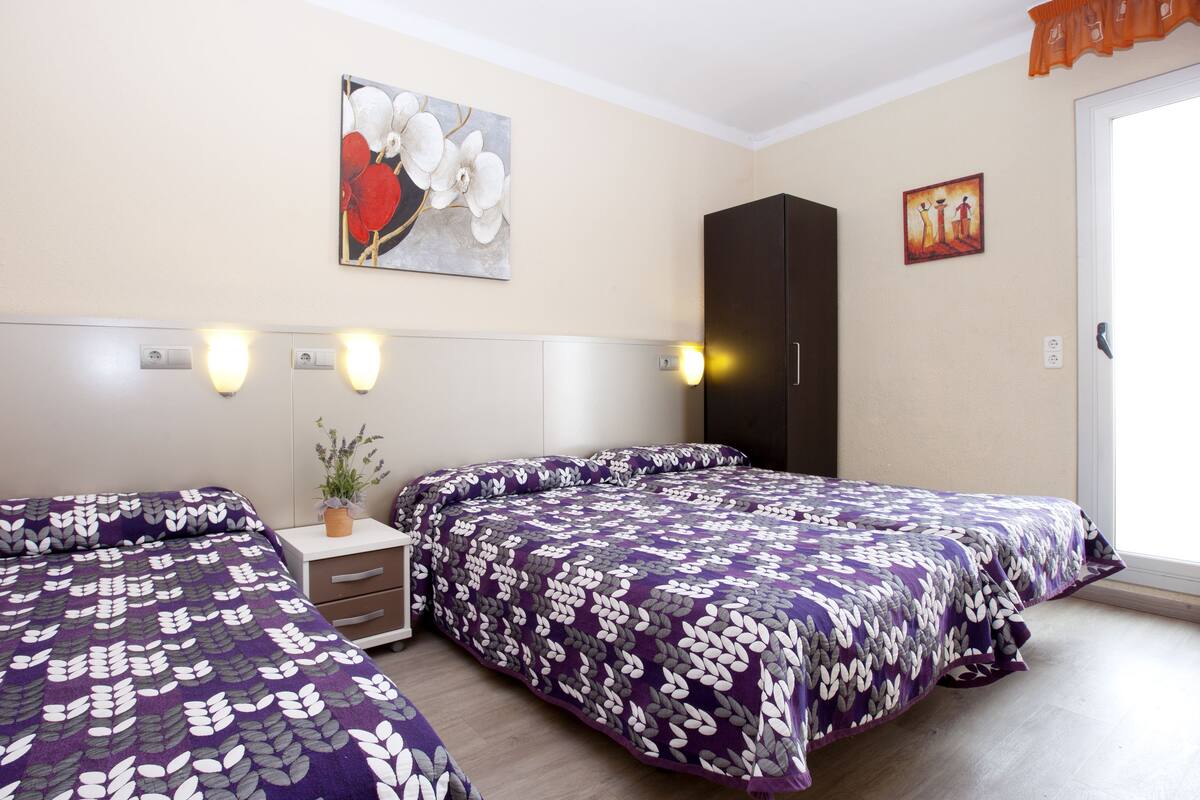 A hotel room with two beds, a wardrobe, a nightstand with a lamp, and a painting on the wall.