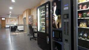 En modern inredning med försäljningsautomater fyllda med snacks och drycker, en reception och en sittgrupp med ett skrivbord och stolar.