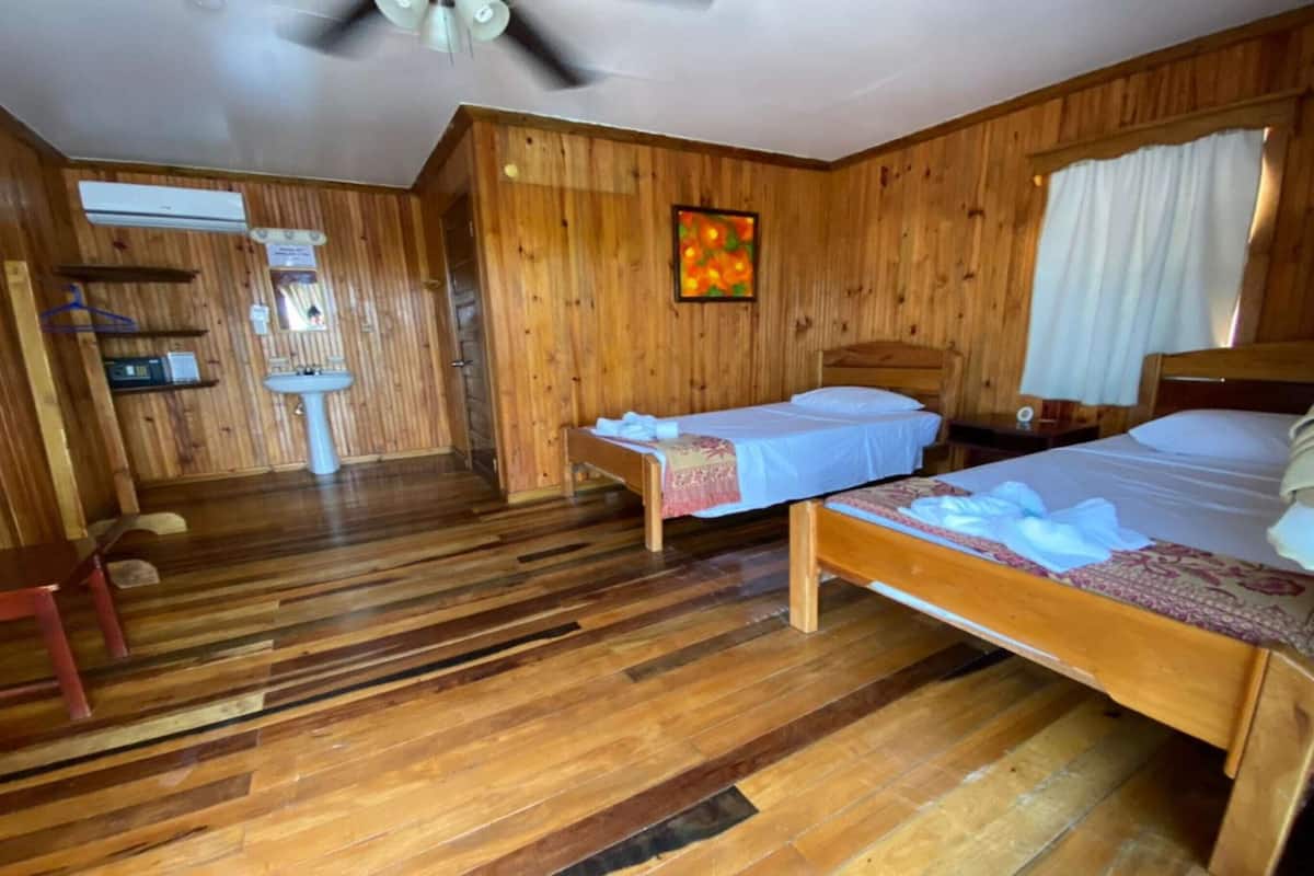 A wooden cabin room with two beds, a sink, and a ceiling fan.