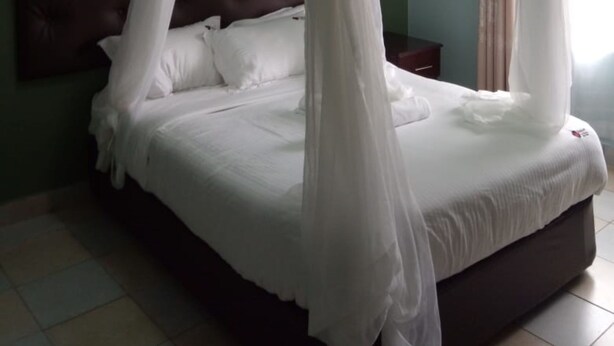 A bedroom with a four-poster canopy bed, a tufted headboard, and a nightstand with a lamp. - Jimlizer Hotel (Nairobi)