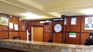 A reception area with a wooden reception desk, a clock, framed certificates, and a sign indicating the reception. - Jimlizer Hotel (Nairobi)