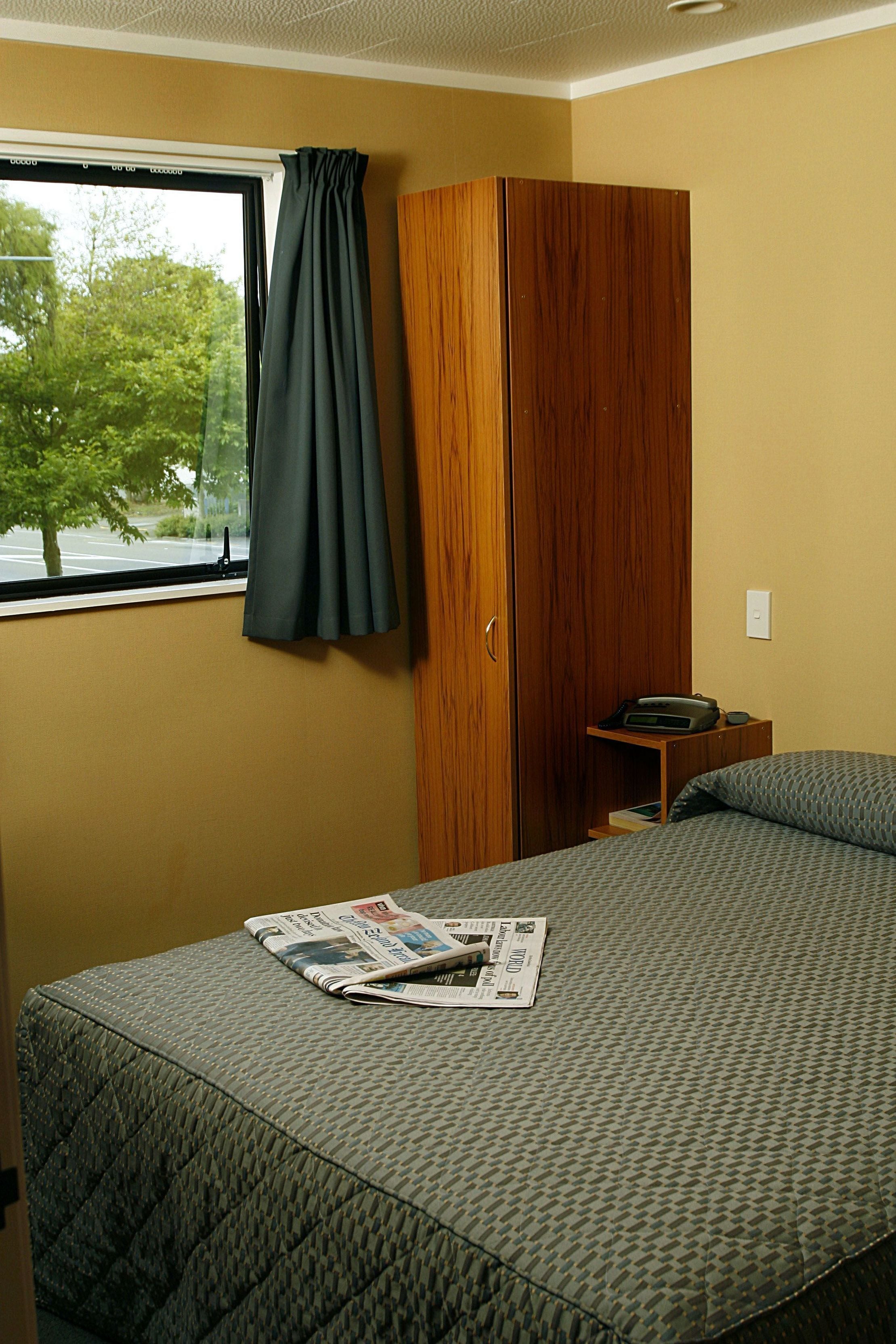 Ein Schlafzimmer mit Bett, Kleiderschrank, einem Fenster mit Vorhängen und Blick auf Bäume.