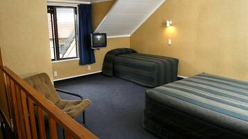 A hotel room with a single bed, a sofa, a chair, a television, and a window with curtains.