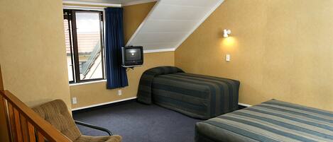 Una habitación de hotel con una cama individual, un sofá, una silla, un televisor y una ventana con cortinas.