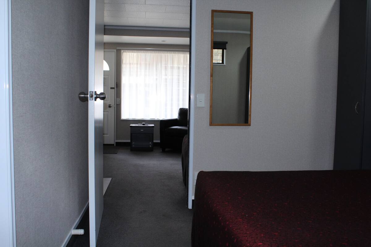 Ein Hotelzimmer mit Bett, Schreibtisch, Stuhl, einem Fenster mit Vorhängen und einem Spiegel an der Wand.