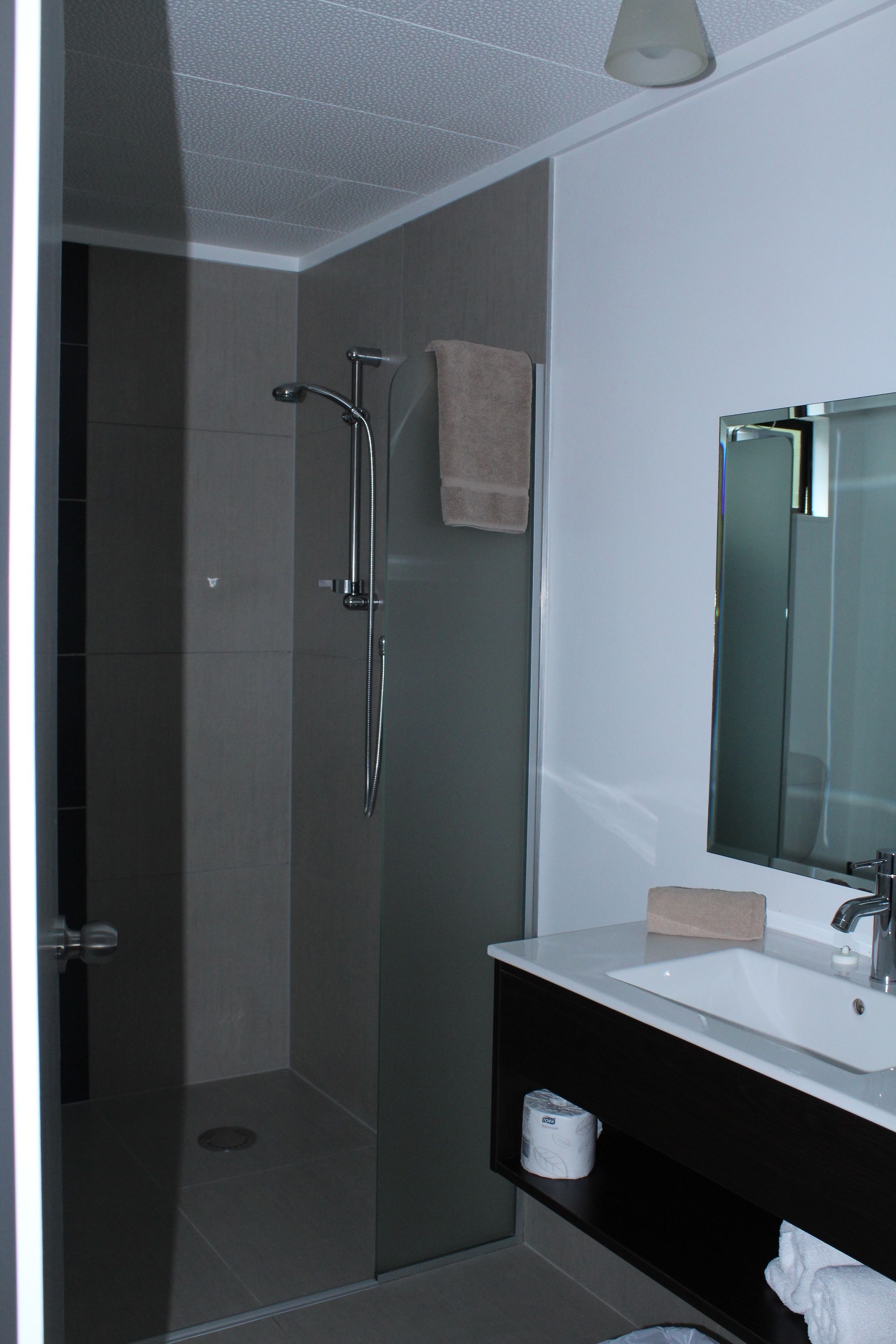 Ein modernes Badezimmer mit einer gläsernen Dusche, einem weißen Waschbecken und einem großen Spiegel.