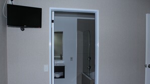 Ein Badezimmer mit Dusche, Waschbecken und Toilette. Ein Fernseher ist an der Wand montiert.