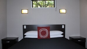 Ein Hotelzimmer mit einem großen Bett, zwei Nachttischen, einem Fenster mit Blick auf Bäume und zwei Wandleuchten.