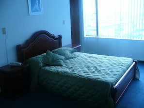 Un dormitorio con cabecera de madera, colcha verde acolchada y mesita de noche con lámpara.