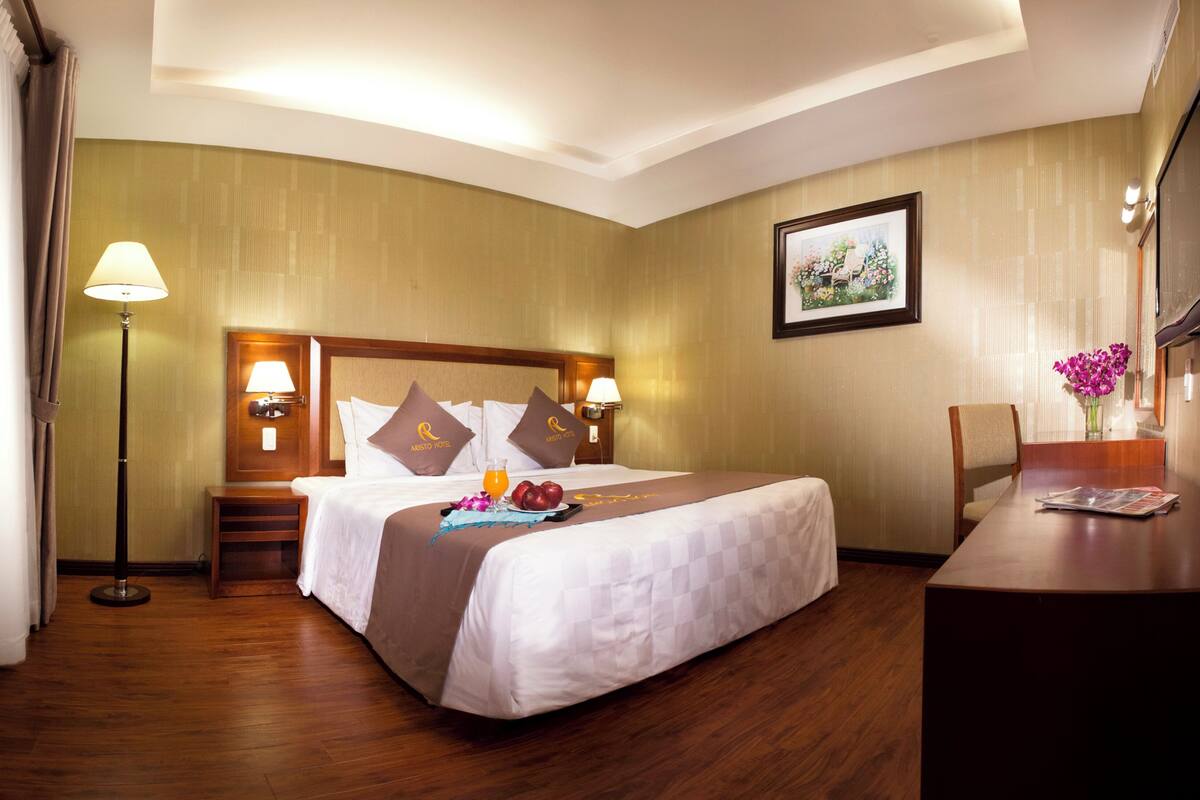 Une chambre d’hôtel avec un grand lit, un bureau, une chaise, une lampe et un tableau au mur.