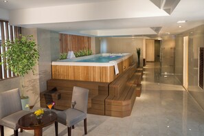 Area benessere moderna con vasca idromassaggio, posti a sedere e un tavolino con un drink.