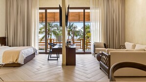 A hotel room with a bed, desk, chair, sofa, and large windows with a view of palm trees and the sea. - Paraiso Rainforest and Beach Hotel (Omoa)