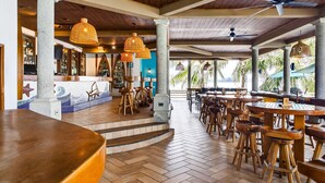 A restaurant with wooden tables and chairs, a bar area, and a view of palm trees. - Paraiso Rainforest and Beach Hotel (Omoa)