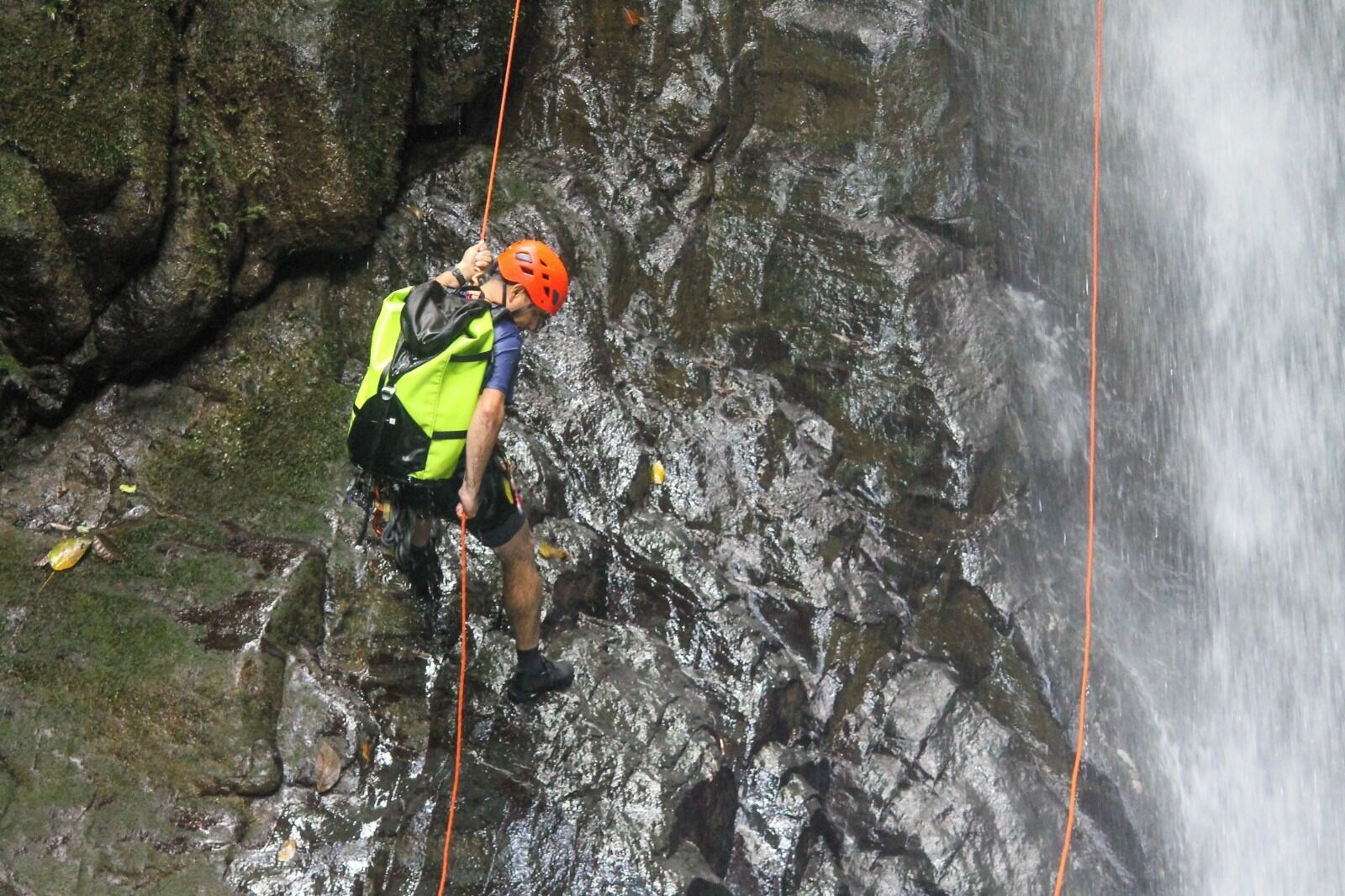 A person rappelling down a rocky cliff with a harness and helmet.
