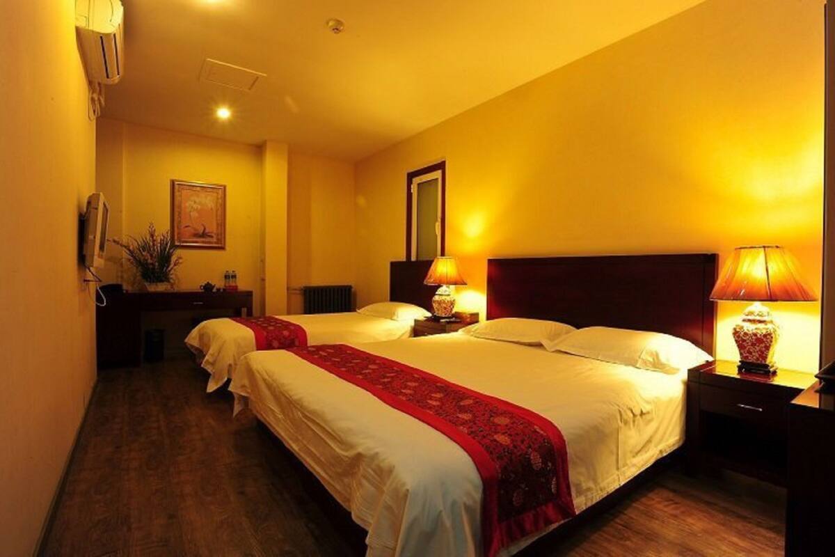 A hotel room with two beds, a desk, a chair, and a lamp.