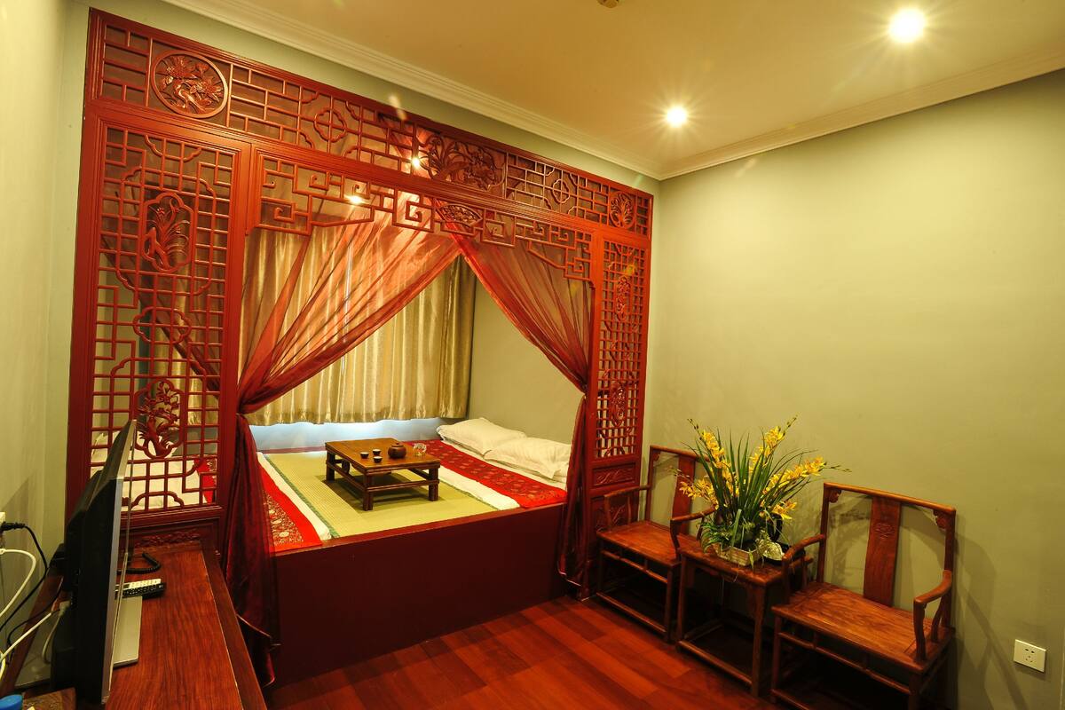 A traditional room with a four-poster bed, a wooden desk, a chair, and a small table with a vase of flowers.