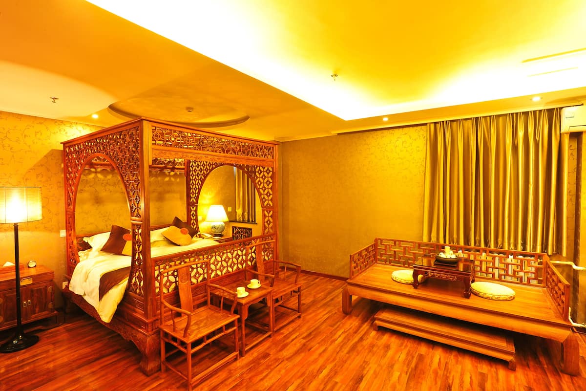 A traditional four-poster bed with a wooden canopy, a small table with a teapot, and a bench with cushions.