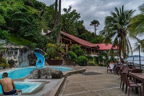 A pool area with a water slide, outdoor seating, and a building with a red roof.