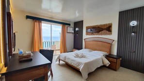A hotel room with a bed, a desk, a chair, a window with curtains, a wall-mounted artwork, and a door.