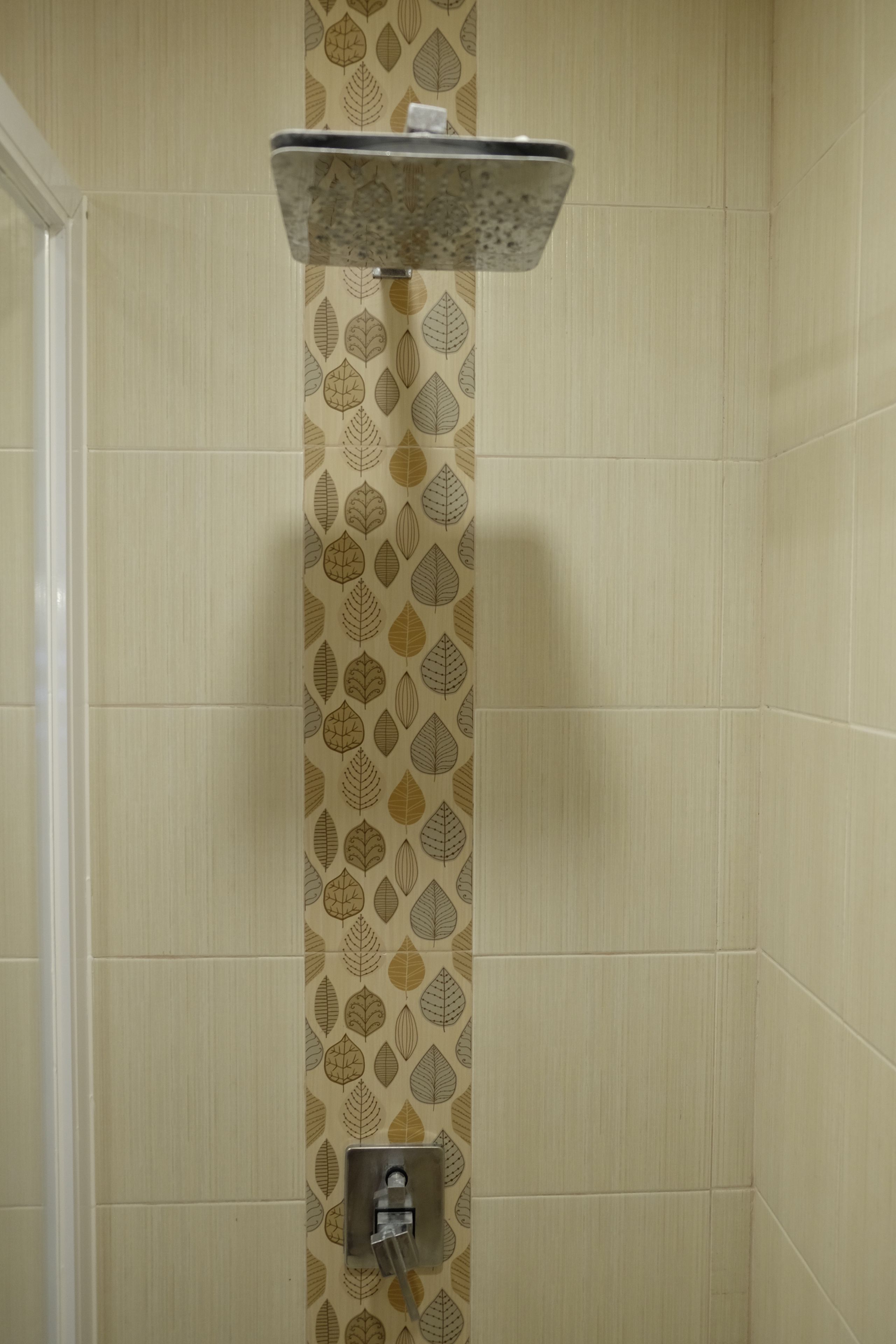 Una ducha con un revestimiento de pared con estampado de hojas, un cabezal de ducha metálico y un panel de control.