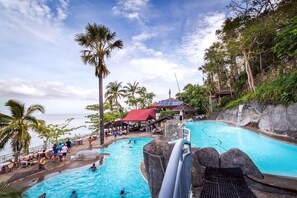 A resort pool area with a waterfall, palm trees, and a view of the ocean.