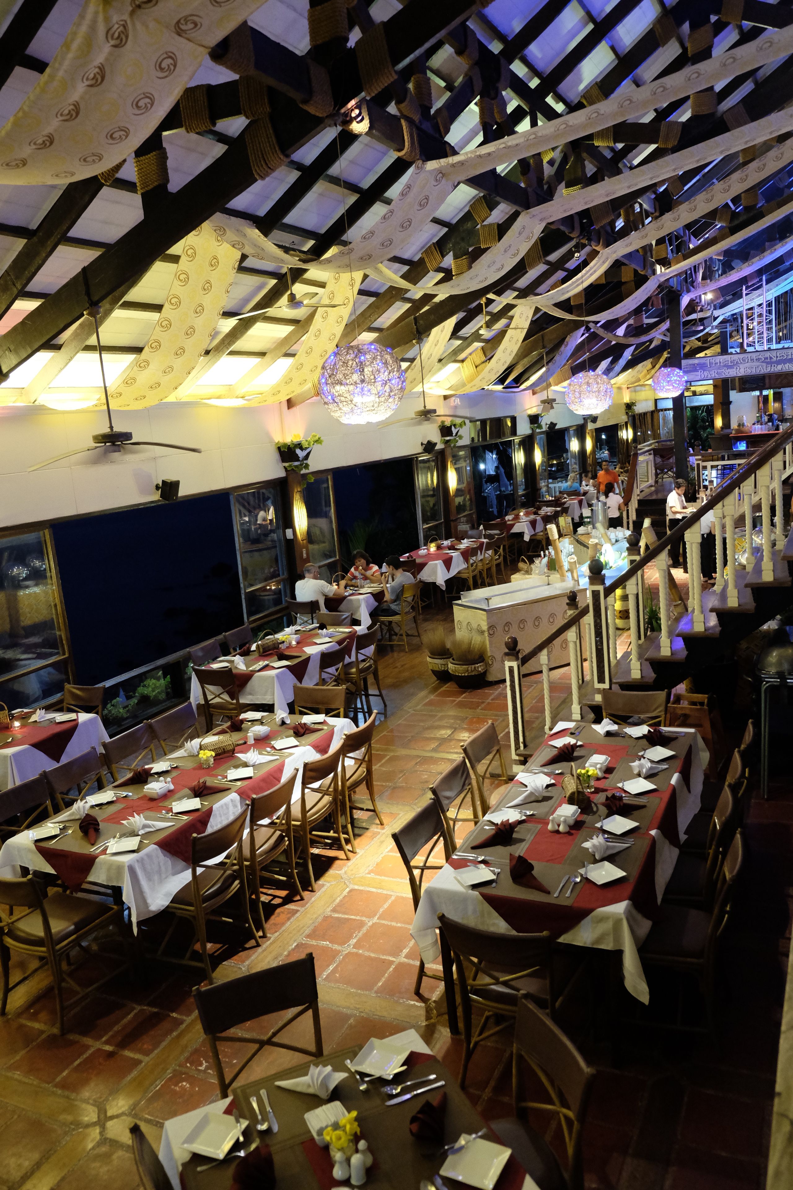 A restaurant with multiple dining tables, chairs, and a staircase leading to an upper level.