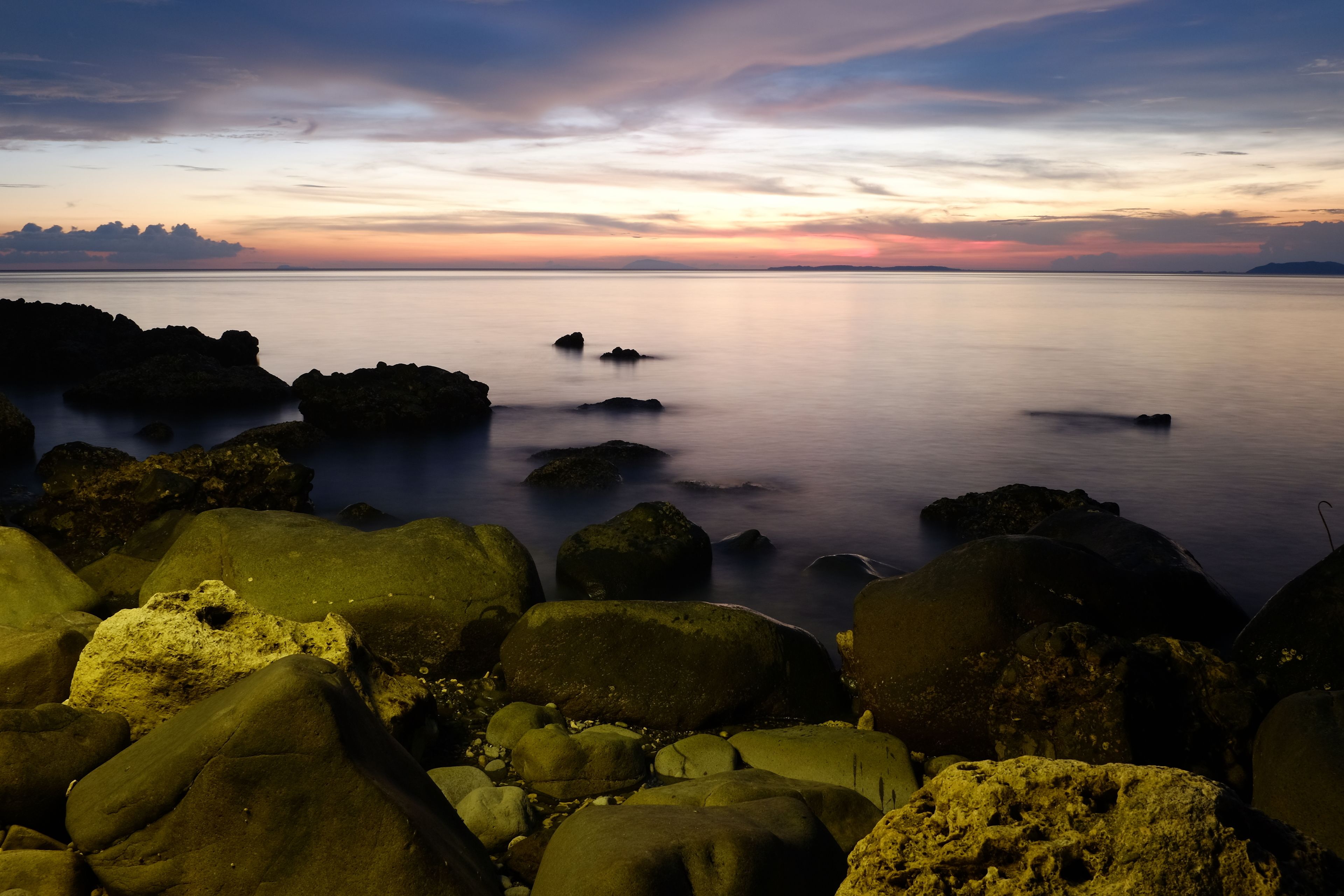 A rocky shoreline with calm water and a sunset sky.