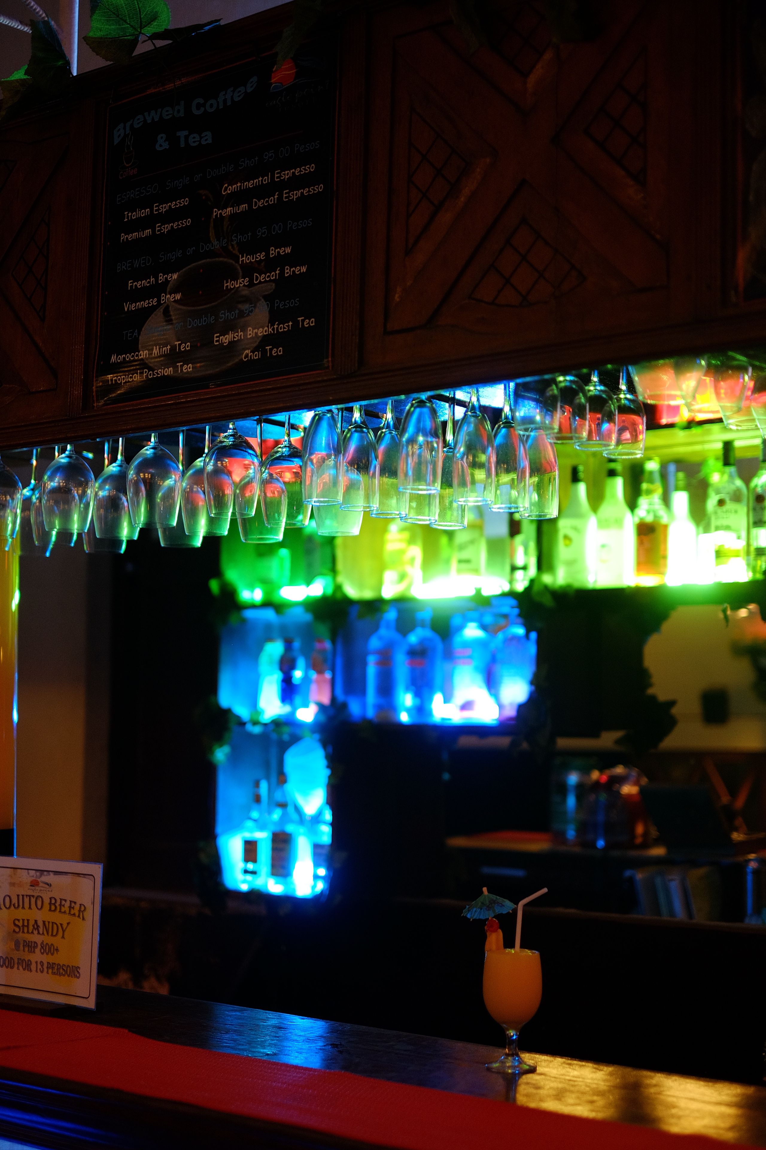 A bar area with a menu for brewed coffee and tea, a glass of a tropical drink, and a sign indicating the beer is shandy.