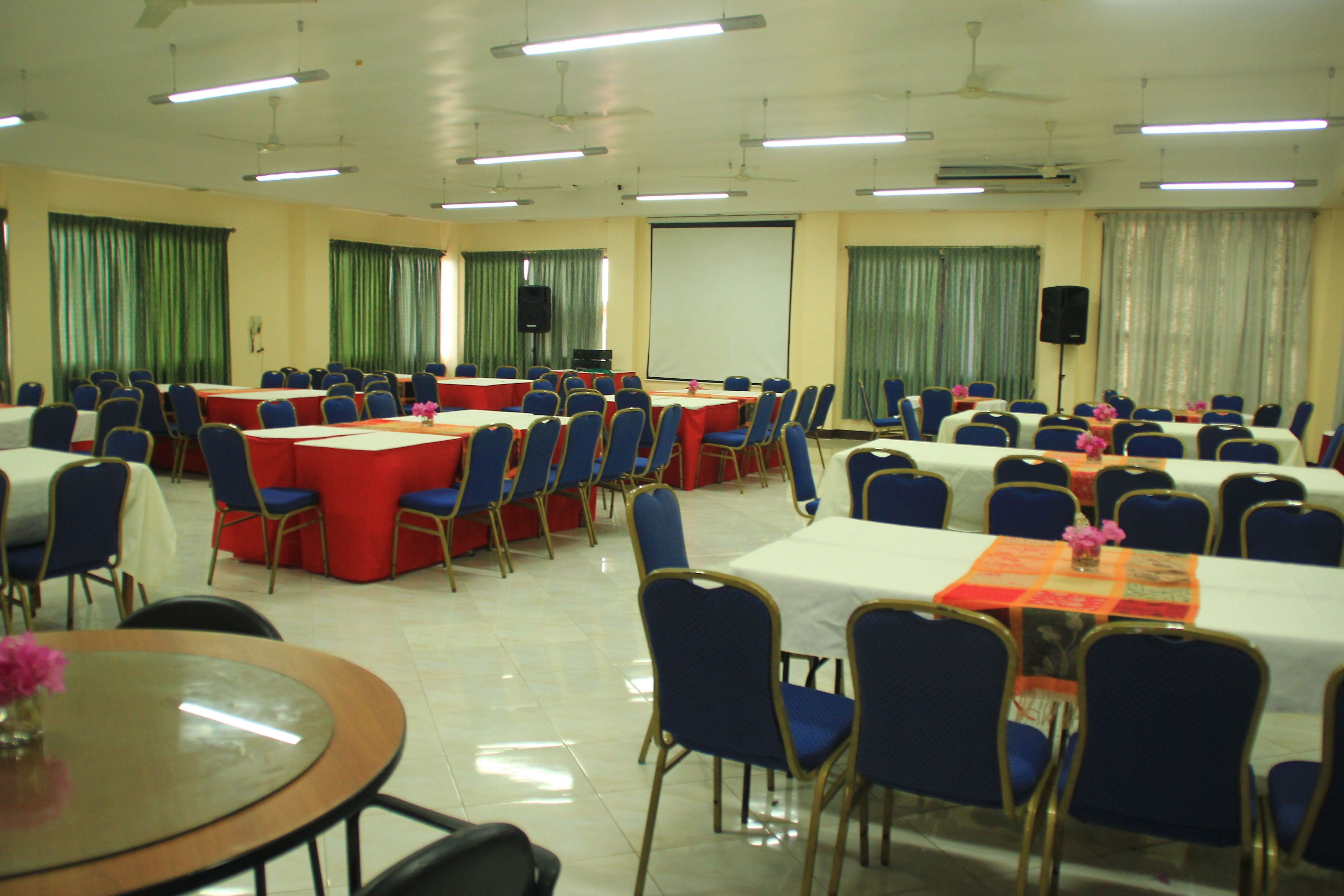 Un salón de conferencias con varias mesas y sillas, una pantalla de proyector y un orador.