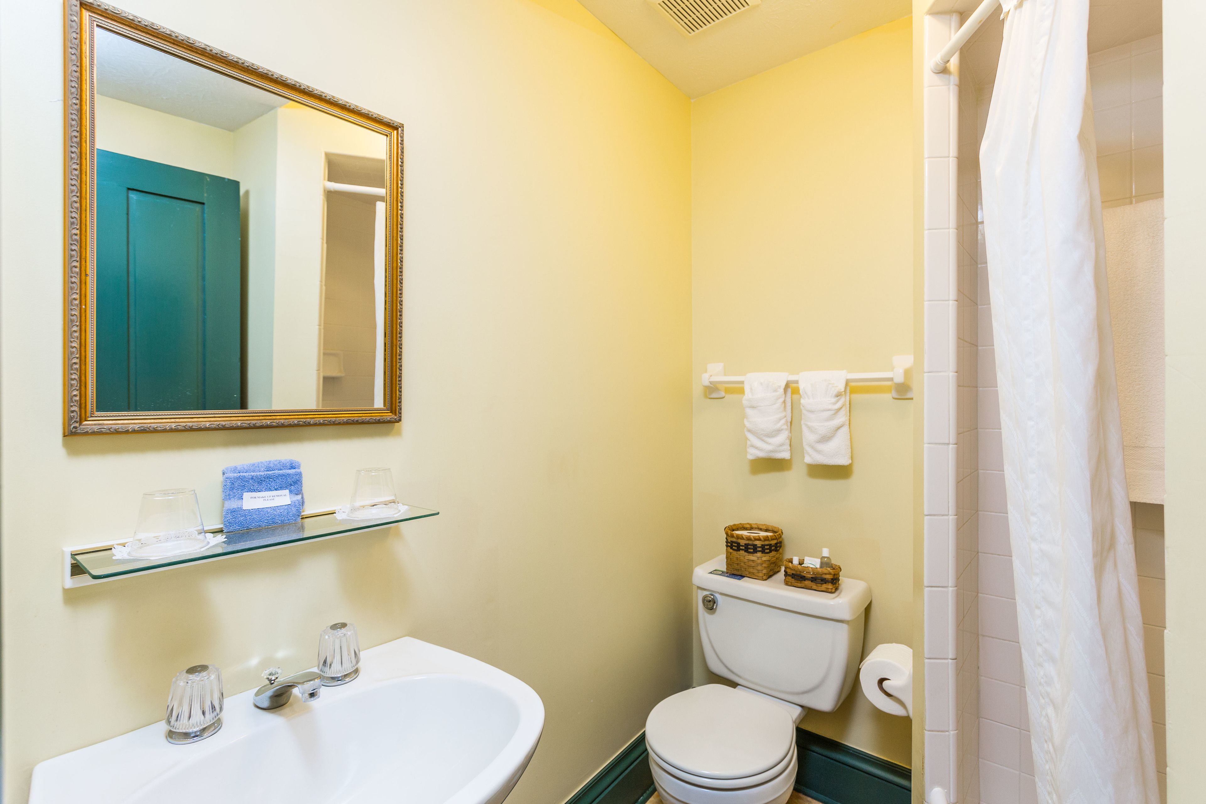 A bathroom with a white sink, mirror, toilet, and shower curtain.