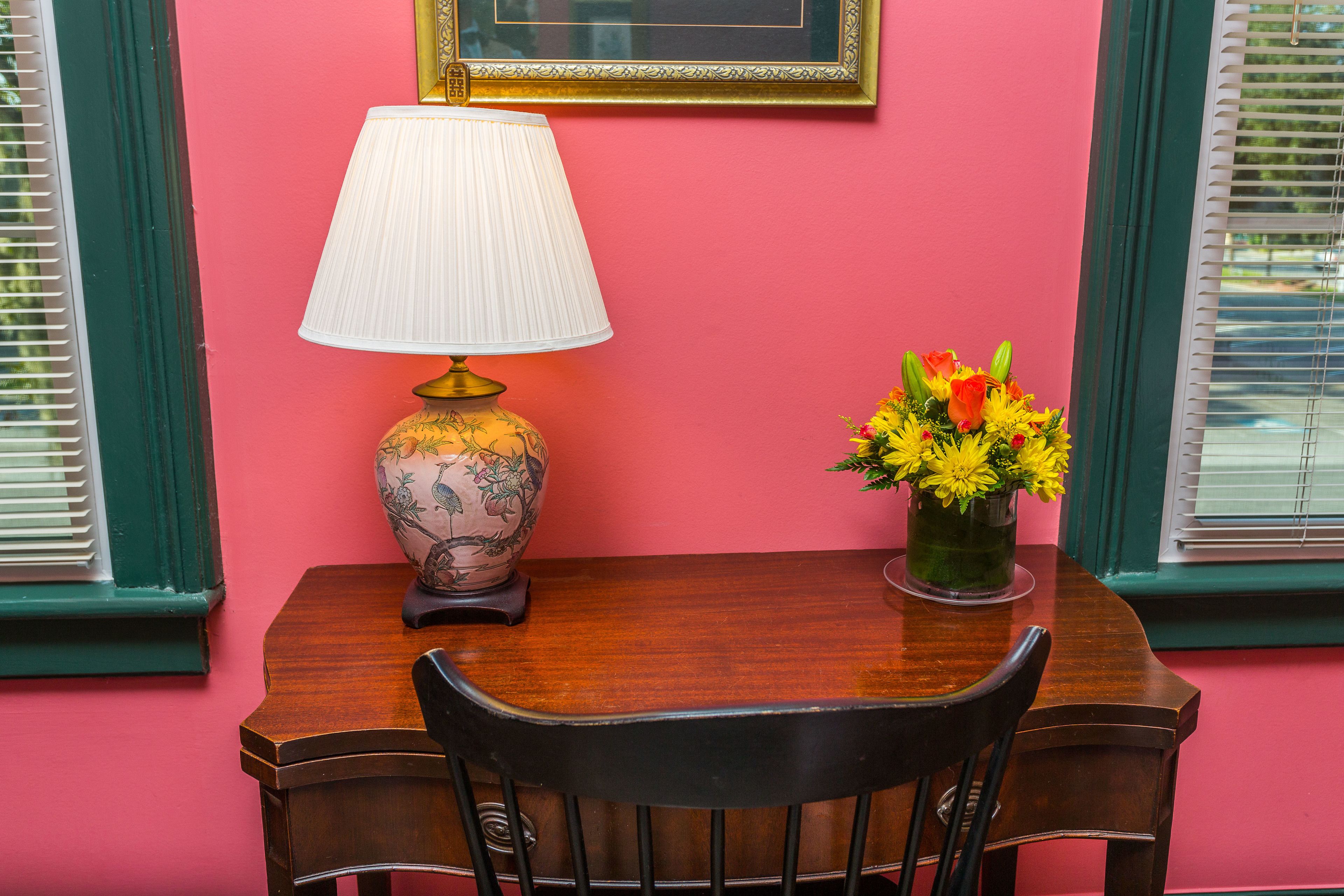 Uma mesa com uma luminária e um vaso de flores em frente a uma parede rosa.