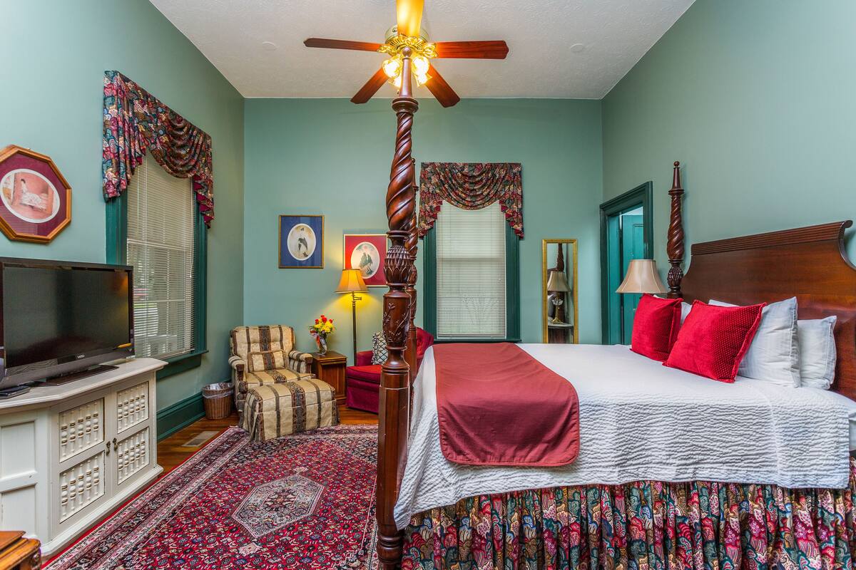 A bedroom with a bed, a television, a chair, and a ceiling fan.