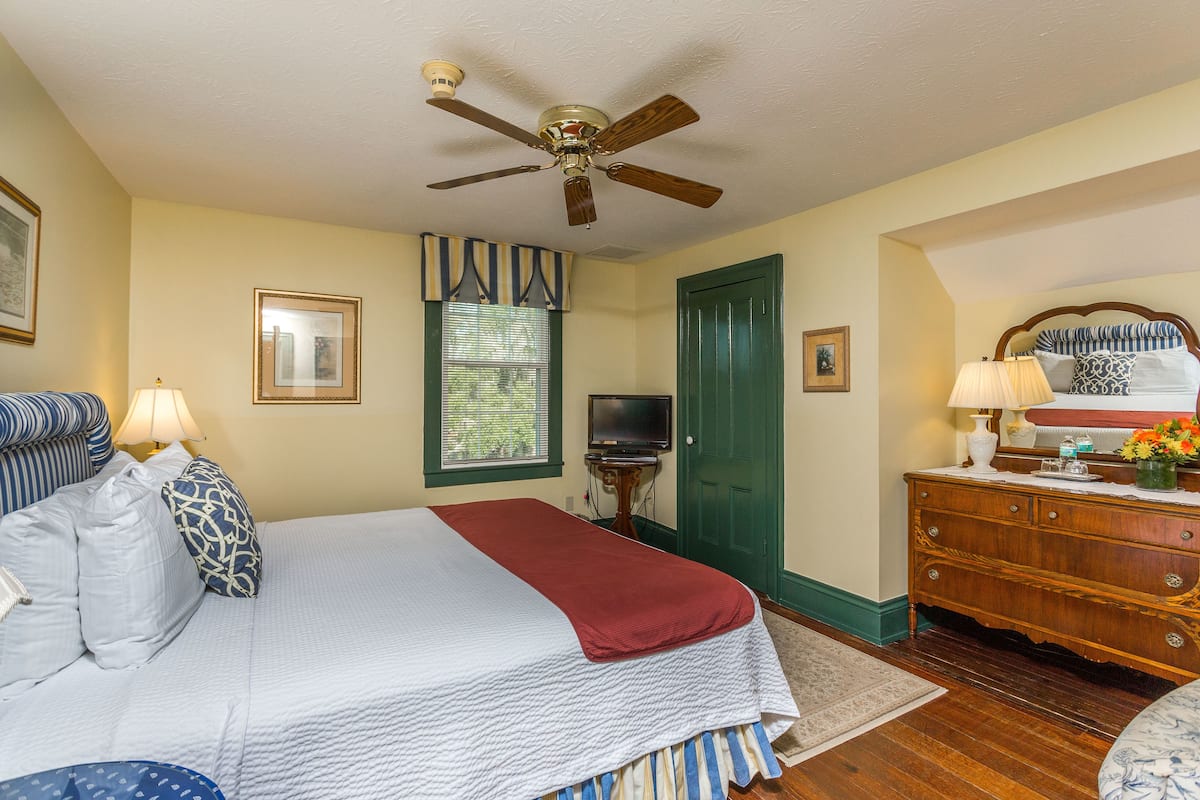 A bedroom with a bed, a dresser, a television, and a ceiling fan.