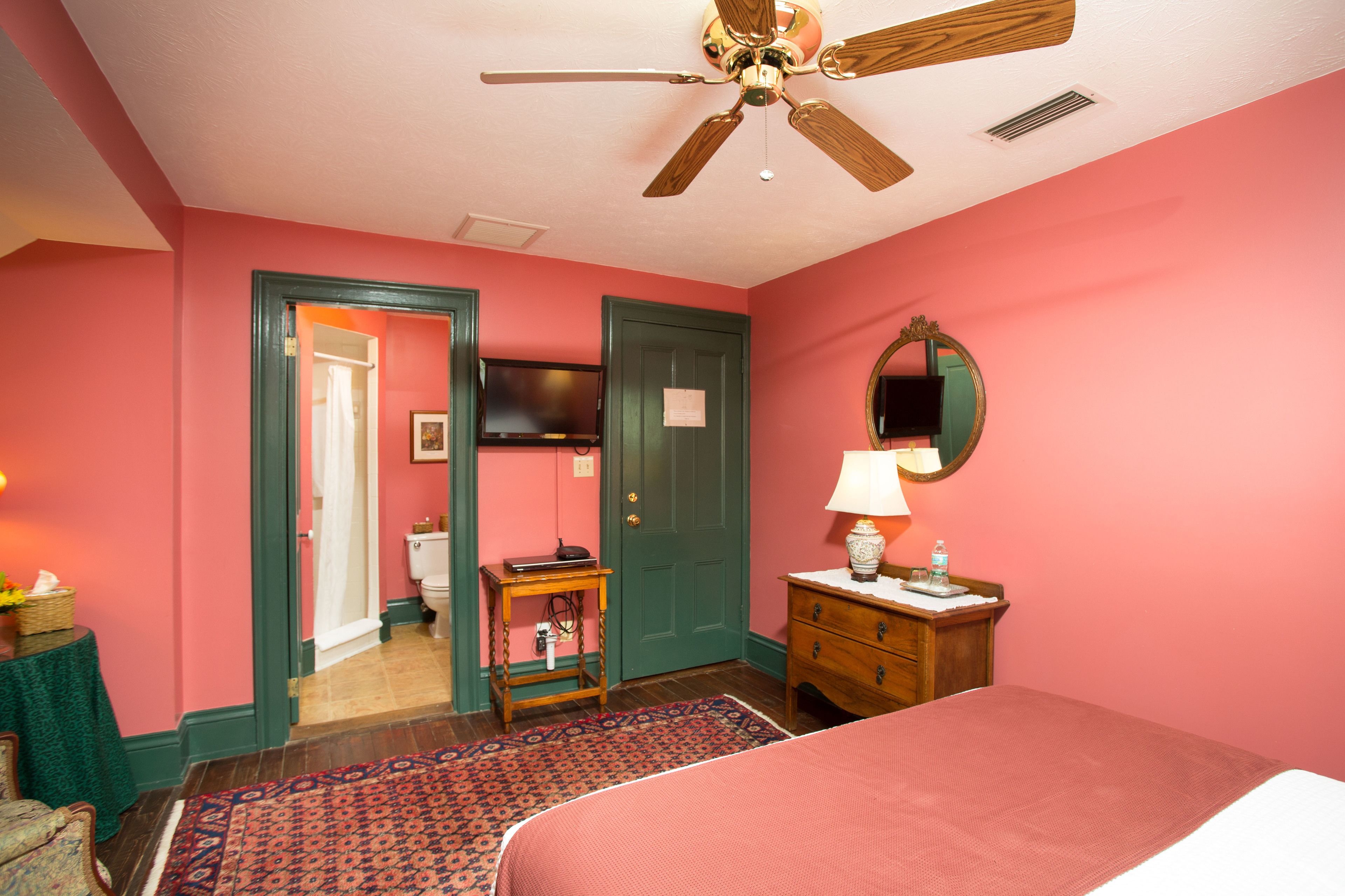 A bedroom with a bed, a dresser, a mirror, a ceiling fan, and a door leading to another room.
