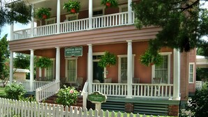 Uma casa de dois andares com varanda, placa indicando ser a Casa Spencer de 1872 e uma cerca branca de piquete.