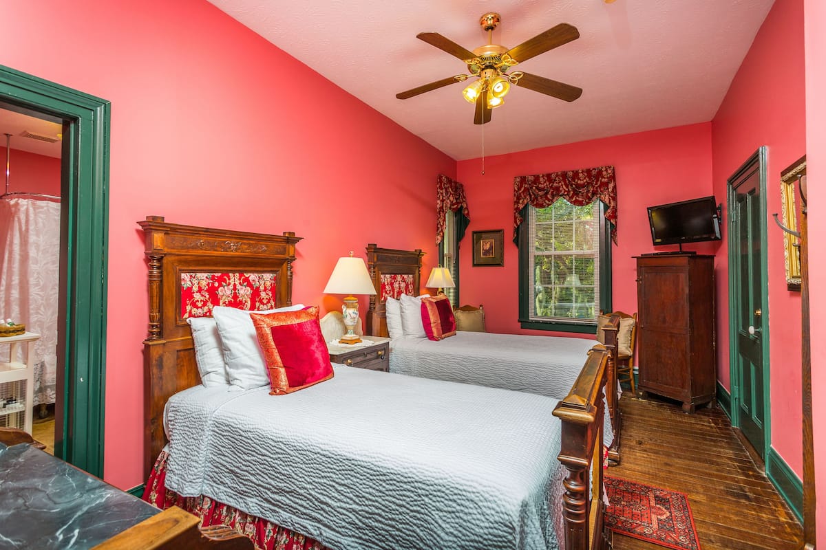 A room with two beds, a ceiling fan, a television, and a wooden cabinet.