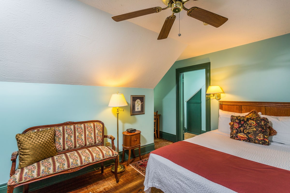 A bedroom with a bed, a wooden ceiling fan, a sofa, and two bedside lamps.