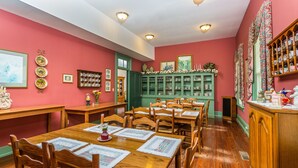 Uma área de refeições com mesas e cadeiras de madeira, armários verdes e quadros nas paredes.