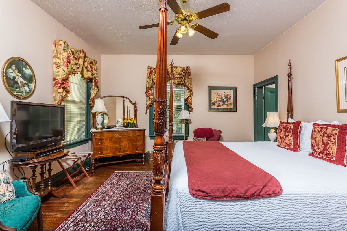 A bedroom with a four-poster bed, a television, a dresser, and a ceiling fan.